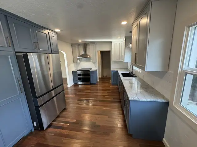 Custom kitchen transformation with slate blue cabinets, stainless refrigerator, marble-look counters and wood floors
