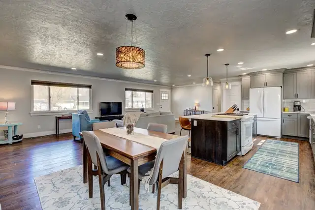 Open dining room and kitchen with a drum pendant over the table, a dark wood island, white cabinets and wood plank floors