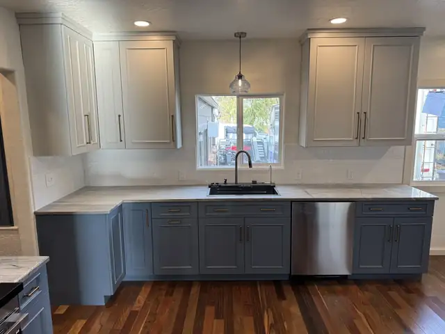 Remodeled kitchen with blue-gray shaker base cabinets, white upper cabinets, a white quartz counter, a pendant over the sink and dark hardwood floors