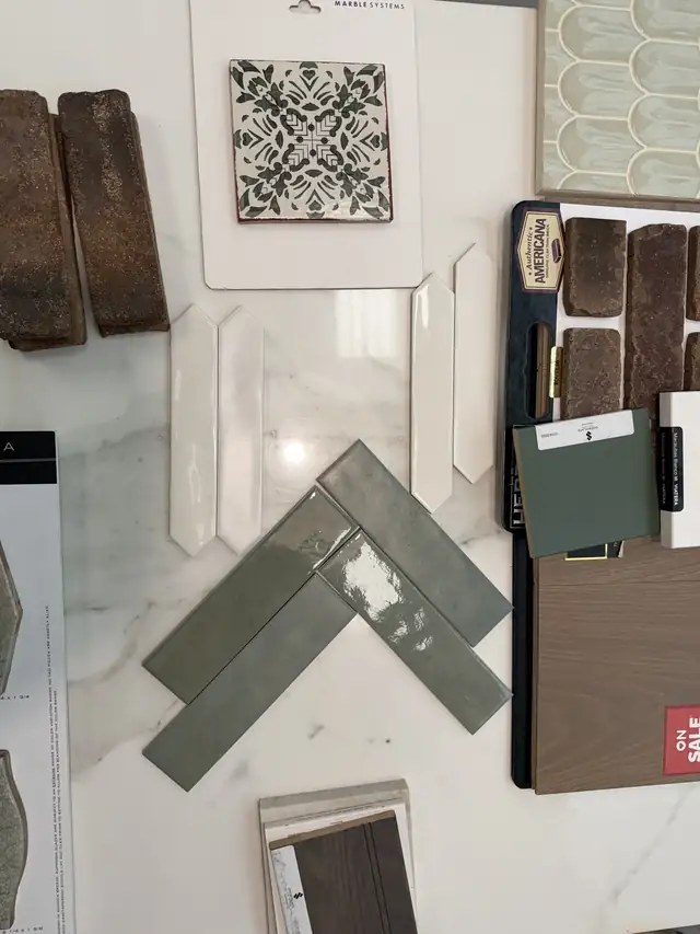 Remodel material selections laid out together: patterned tile, green herringbone tile, brick, quartz and wood finish samples