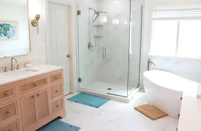 Bathroom remodel with natural wood vanity, brass fixtures, marble-look frameless glass shower and freestanding tub