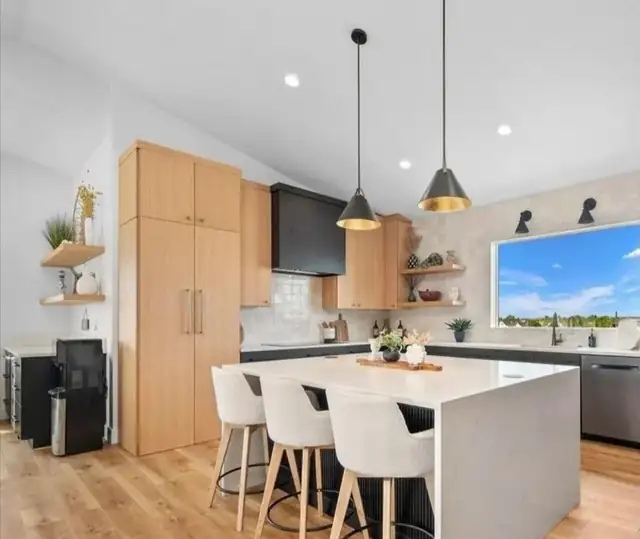 Light oak kitchen with white waterfall island, black hood, open wood shelves and brass pendant lights