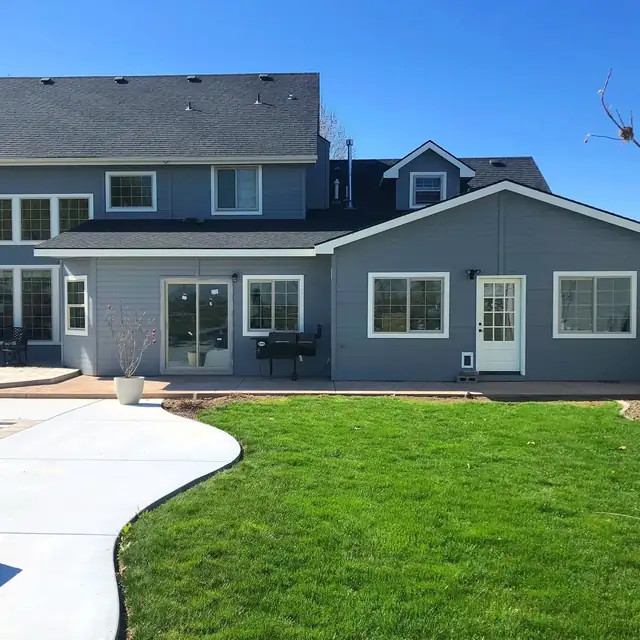 Rear of a gray-sided home with a single-story addition, new windows, patio door and curved concrete walkway