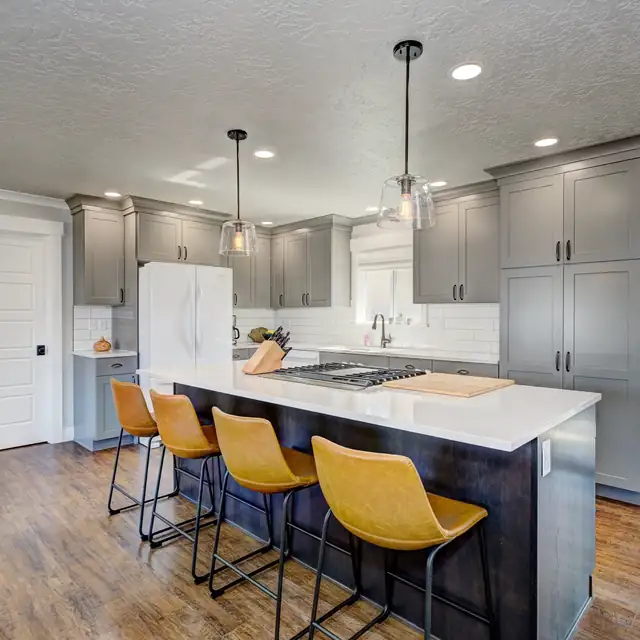 Kitchen island with navy base, white quartz top and four mustard leather bar stools under glass pendants